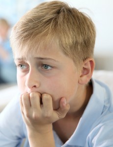 12-year-old boy sitting in couch at home, parents in background